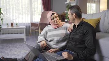 Muslim woman wearing hijab and her husband looking at laptop at home. Muslim couple talk while looking at laptop at home. video