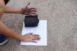 de cerca chico sellado su sucio mano con negro manchar de carbón en blanco papel, hacer mano impresión pintada. concepto, aprendizaje por haciendo. toque y observar en Ciencias tema actividad. naturaleza combustible foto