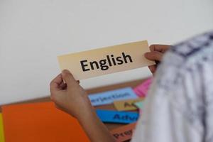 Closeup student's hands  hold English word card. Concept, education, learning and studying language. Education. Reading and memorizing strategy of learning process for kid. Practice makes perfect. photo