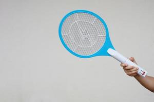 Closeup hand holds mosquito electric swatter racket. Concept, electric device to kill mosquitoes, insects, bugs by swatting to flying insects. photo