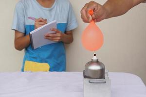 Balloon with water filled is burned on fire flame of metal lantern. Student observe and take note on paper notebook. Concept, science experiment. Fireproof balloon demonstration. Learning by doing. photo