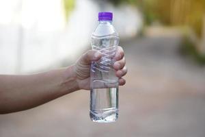 Closeup hand holds drinking water bottle with purple cap. Concept , Drinking water for health, Healthy lifestyle. Quenching thirst, reduce fatigue, refresh body. photo