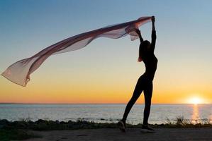 Silhouette slender girl at sunset on seashore rejoices with a transparent cloth photo