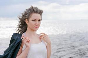 Young stylish woman in light light T-shirt and leather jacket and curly hair photo