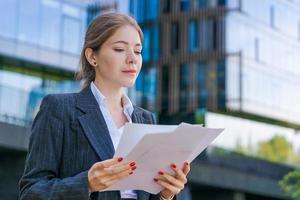 Elegant caucasian business woman in formal wear holds paper documents in her photo