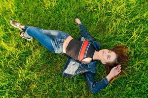 Young Woman lying in nature on green grass in park, relaxing smiling, her red photo