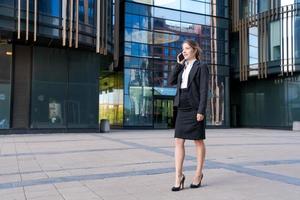 Smiling business woman in suit standing on city street against backdrop photo