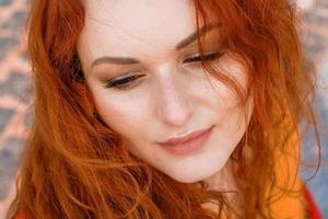 Close-up portrait young caucasian woman with red curly hair in red coat in wind photo