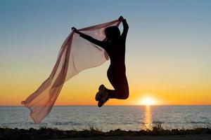 Silhouette slender girl at sunset on seashore rejoices with a transparent cloth photo