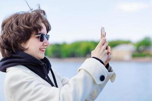 Young woman on vacation using mobile phone to take pictures river and city photo