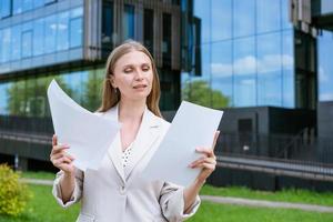 Business woman successful executive director, reads paper documents in a light jacket, standing on the street near photo