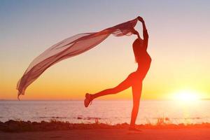 Silhouette slender girl at sunset on seashore rejoices with a transparent cloth photo
