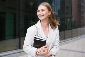 Successful business woman holds a notebook in her hand in front of an office building. Pretty photo