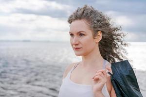 Young stylish woman in light light T-shirt and leather jacket and curly hair photo