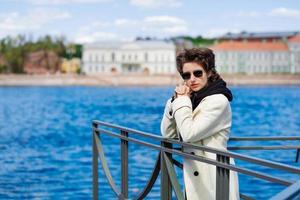 Beautiful young woman walks along embankment in white coat and black sweatshirt photo