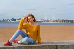 Young red-haired girl in yellow sweater and jeans. Pretty woman sits photo
