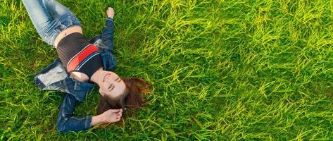 joven mujer acostado en naturaleza en verde césped en parque, relajante sonriente, su rojo foto