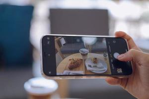 mujer tomando un imagen de comida con un móvil teléfono en un café foto