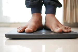young man's feet on weight scale top view photo