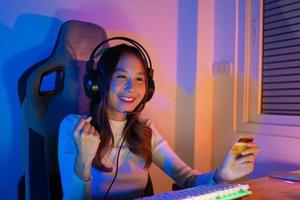 Top up online game with credit card concept. Gamer and E-Sport online of Asian woman playing online computer video game with lighting effect, broadcast streaming live at home. Gamer and E-Sport gaming photo