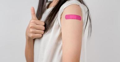 Young woman thumb up sign after getting a vaccine. showing shoulder arm with bandage after receiving vaccination, herd immunity, side effect, booster dose, vaccine passport and Coronavirus pandemic photo