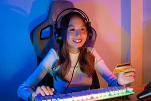 Top up online game with credit card concept. Gamer and E-Sport online of Asian woman playing online computer video game with lighting effect, broadcast streaming live at home. Gamer and E-Sport gaming photo