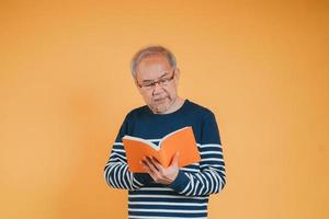 Happy positive senior male smiling and read book education knowledge learning on color background. photo