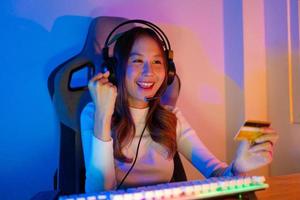 Top up online game with credit card concept. Gamer and E-Sport online of Asian woman playing online computer video game with lighting effect, broadcast streaming live at home. Gamer and E-Sport gaming photo