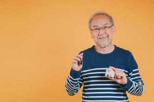 Senior male holding wooden house model property owner after retirement on yellow background. photo