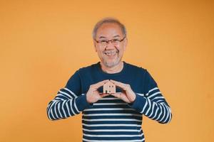 Senior male holding wooden house model property owner after retirement on yellow background. photo