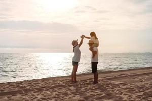 contento asiático familia disfrutar el mar playa a consistente padre, madre y hija teniendo divertido jugando playa en verano vacaciones en el Oceano playa. contento familia con vacaciones hora estilo de vida concepto. foto