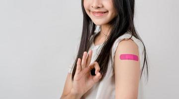 Happy young woman show ok sign after getting a vaccine. showing shoulder with bandage after receiving vaccination, herd immunity, side effect, booster dose, vaccine passport and Coronavirus pandemic photo
