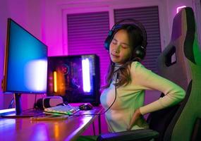 Young people Backache. Gamer and E-Sport online of Asian woman playing online computer video game with lighting effect, broadcast streaming live at home. She a backache due to sitting for a long time photo