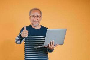 asiático mayor hombre utilizando ordenador portátil computadora para trabajando después Jubilación en el amarillo antecedentes. foto