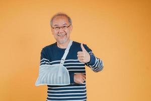 Arm broken. Senior male sling support hand confident smile broken after accident wear arm splint for treatment show good sign. health insurance on mobile concept. photo