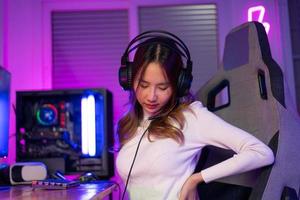 Young people Backache. Gamer and E-Sport online of Asian woman playing online computer video game with lighting effect, broadcast streaming live at home. She a backache due to sitting for a long time photo