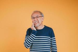 Dental pain. Portrait senior old man sad hand touching cheek suffering from toothache studio shot isolated on yellow background, Asian unhappy elder man problems with teeth pain, dental healthcare photo