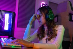 ojos cansado. jugador y e-sport en línea de asiático mujer jugando en línea computadora vídeo juego con Encendiendo efecto, transmitir transmisión En Vivo a hogar. su ojos fueron cansado foto