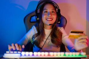 Top up online game with credit card concept. Gamer and E-Sport online of Asian woman playing online computer video game with lighting effect, broadcast streaming live at home. Gamer and E-Sport gaming photo
