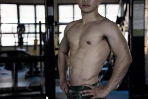 Sexy body of muscular young soldier Asian man in gym. Concept of health care, exercise fitness, Strong muscle mass, body enhancement, fat reduction for men's health supplement product presentation. photo