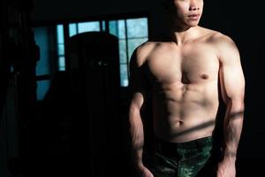 Sexy body of muscular young soldier Asian man in gym. Concept of health care, exercise fitness, Strong muscle mass, body enhancement, fat reduction for men's health supplement product presentation. photo