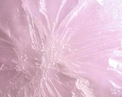 Close-up image of transparent melted plastic cellophane film on pink background.