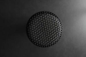 Close-up shot, the top of the microphone against a black background with studio lighting in the same tone. photo