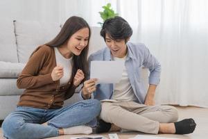 Happy excited, smiling asian young couple love, wife and husband hold paper letter, reading paperwork document getting, receive job promotion, tax refund or loan mortgage approval, good news by mail. photo