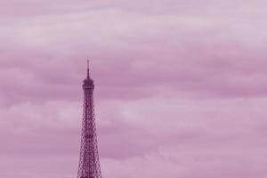 top part of Eiffel Tower in Paris against clouds colored in pink