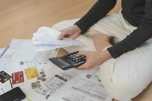 financiero deber asiático mujer, hembra sentado en piso hogar, estresado y confuso por calcular gastos desde factura o factura, tener No dinero a pagar, hipoteca o préstamo. deuda, bancarrota o arruinado concepto. foto