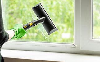 woman washes the windows of a house with a steam generator. To clean up the house in the spring. House cleaning. photo