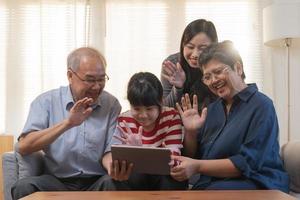 Happy family asian aged grandfather, grandmother have fun, smiling parent, girl using touchpad watching funny video call, play games and take photo selfie enjoy weekend together in living room at home