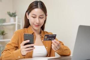 Convenience online internet banking, asian young woman hand in holding credit card to payment spending by scan qr code to transfer or pay money without cash at home. Technology of financial. photo