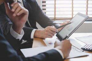 Business meeting, two caucasian, asian group man use tablet brainstorm analyzing on graph data of cost plan or document, paperwork and discussing in board room on table. People working conference room photo